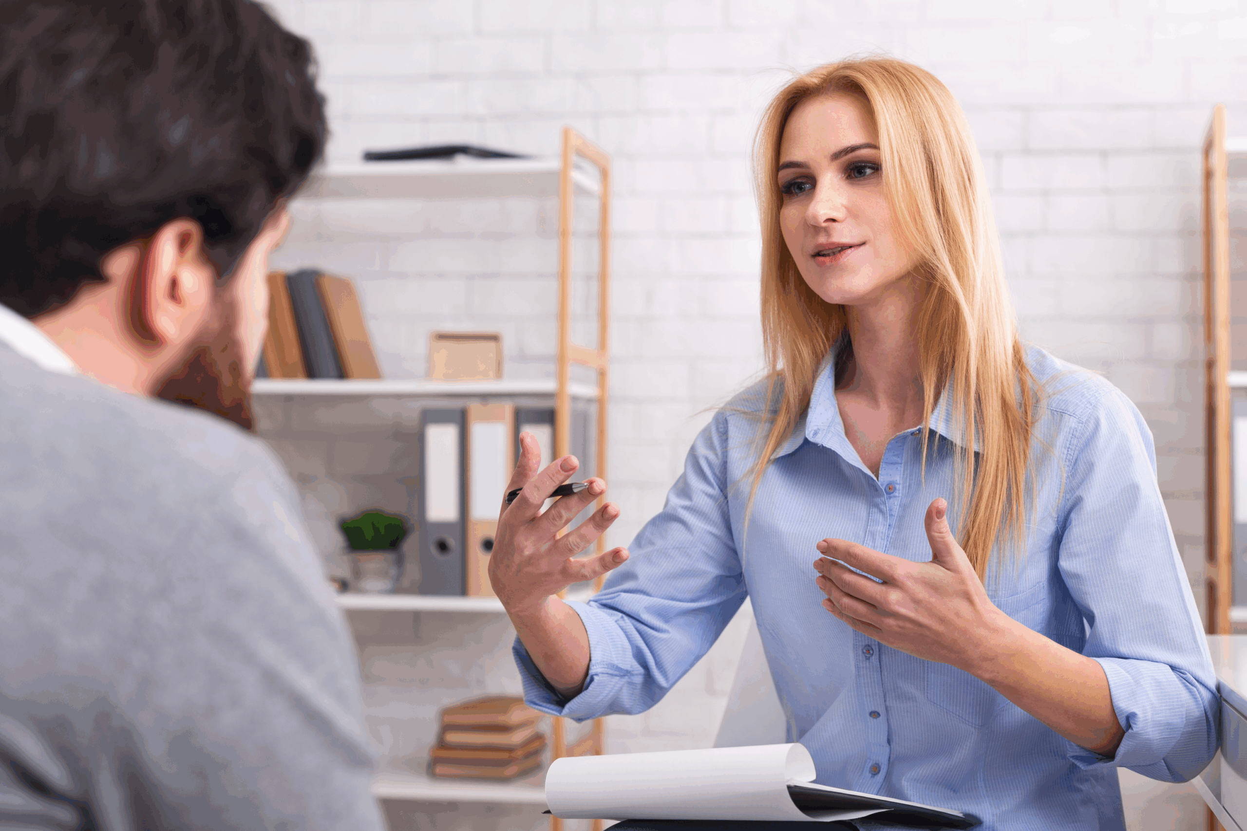 A Blond Woman in a Blue Blouse Speaks with a Man in an Office