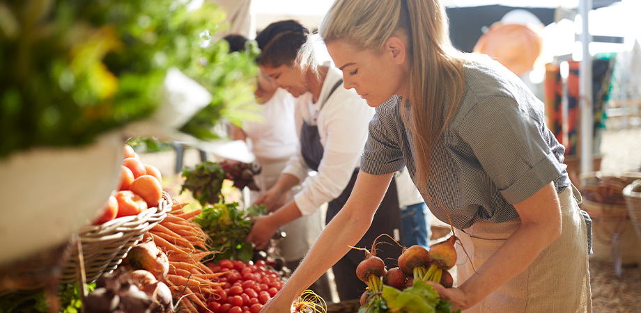 Young woman selects vegetables at an open air market.