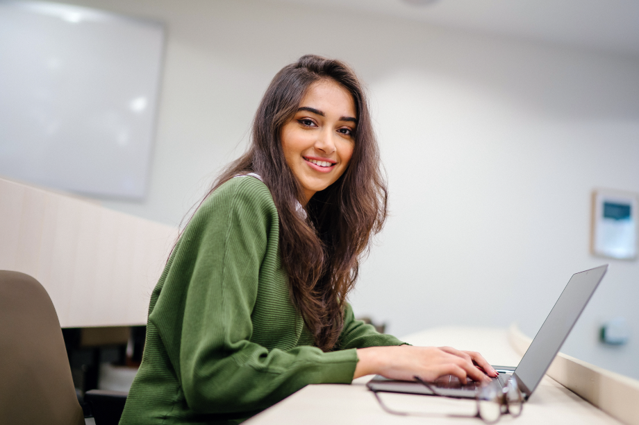 A student in a green sweater works on her laptop in class.