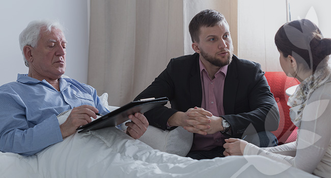 Social worker speaking with cancer patient and family member next to hospital bed.