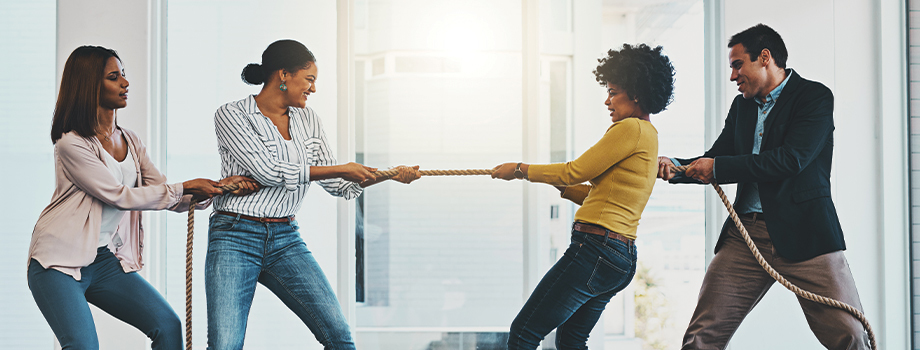 Colleagues in literal a game of tug-of-war with a rope in the office.