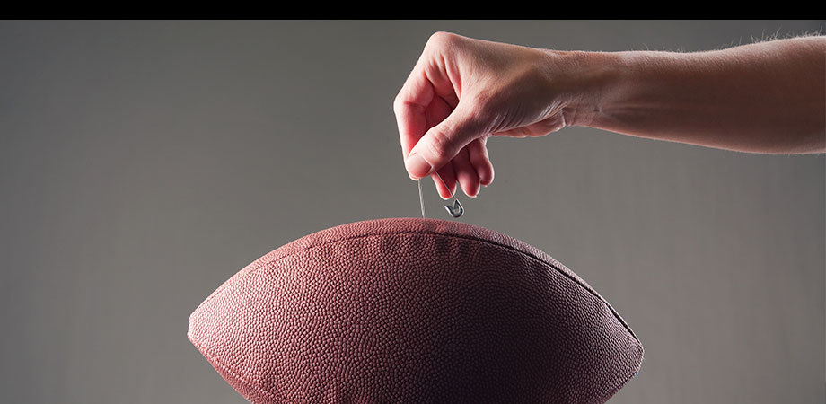 Hands holding a football while deflating it.