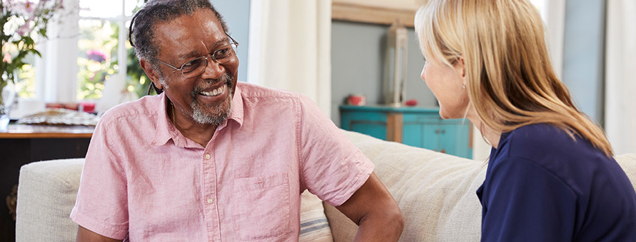 Older client sits on a sofa having a discussion with his social worker.